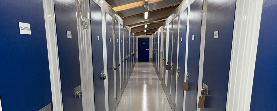 A hallway of self storage units with blue doors, featuring secure padlocks.
