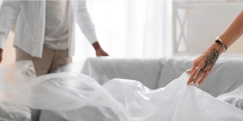Two people wrapping a couch in a plastic dust cover